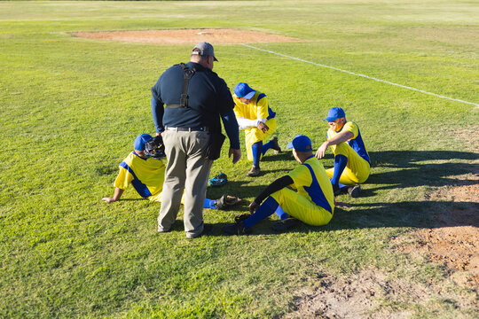 Coach and male teen baseball players gathering on sunlit infield diamond with gloves and helmets