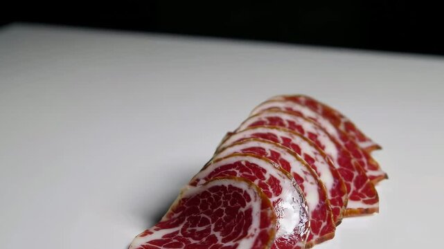 Sliced cured meat rotating on dark background with dramatic lighting