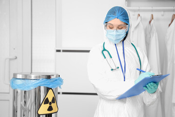 Medical worker in protective uniform and with container for radioactive waste in clinic