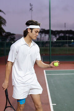 Male tennis player serving on tennis court wearing headband and kinesiology tape with racket, ball