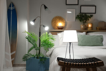 Glowing lamps on coffee table with houseplants and surfboard near bed in bedroom at night