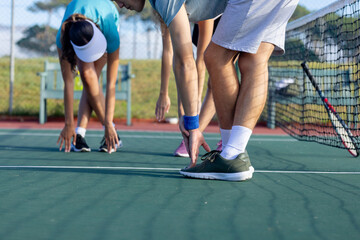 Diverse tennis partners stretching by bending forward on green hardcourt near net and racket