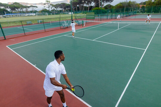 Diverse male tennis players playing doubles match on green court with rackets near net, copy space