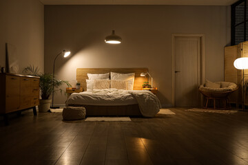 Interior of dark bedroom with tables, armchair and glowing lamps