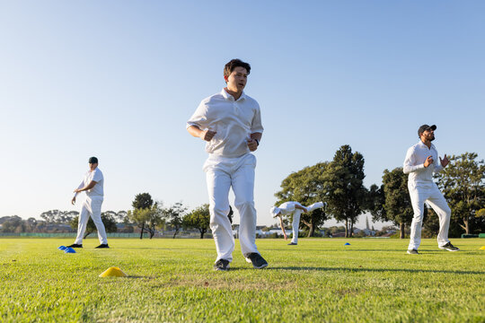 Diverse male cricket teammates jogging between yellow and blue training cones on grass field - Powered by Adobe
