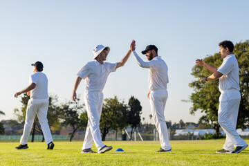 Male cricket teammates in uniforms and caps high-fiving on grassy field around blue training cone