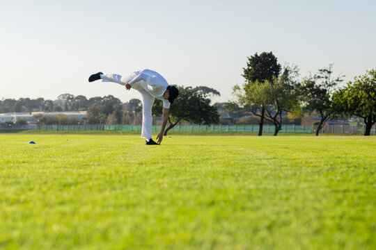 Indian man wearing cap balancing on leg on grass field beside blue cone, copy space