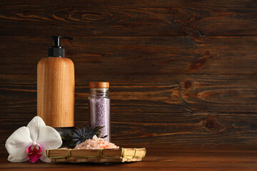 Beautiful spa composition with tray of sea salt, flowers and bottle of cosmetic product on brown...