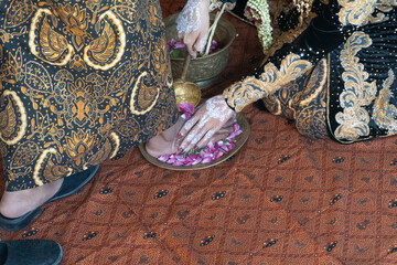 Fototapeta premium Close-up of a traditional Indonesian wedding ritual, showing feet, hands with white henna, and floral offerings.