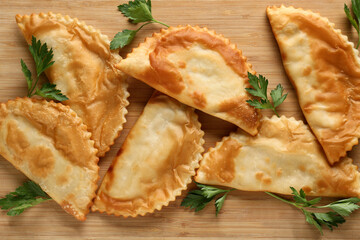 Wooden cutting board with tasty chebureks and fresh parsley, closeup