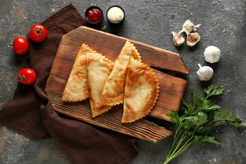 Board with tasty chebureks, fresh vegetables and sauces on black grunge table