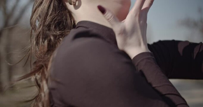 A young woman dances freely in a park on a sunny day, expressing joy and peace through her movements. Her black turtleneck and silver hoop earrings complement her graceful performance.