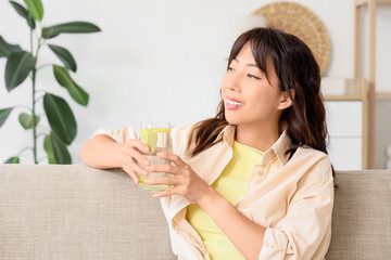 Young Asian woman with citrus infused water sitting on sofa at home