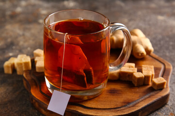 Cup of hot tea with sugar cubes and ginger on grunge background