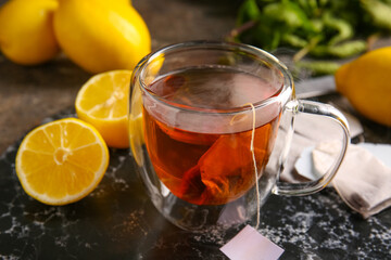 Cup of hot beverage with tea bags and lemons on grunge background