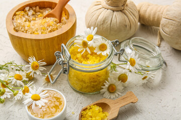Chamomile flowers, glass jar, bowl and scoop with sea salt on grey grunge background, closeup