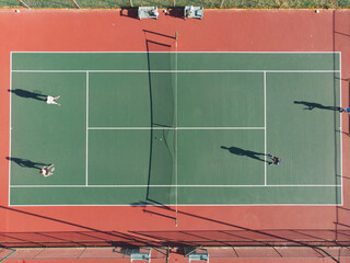 Diverse male players competing in doubles tennis on green court holding rackets near net and ball