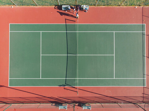 Diverse friends gathering around cart and bench with rackets and water bottles on tennis court