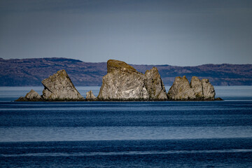 A scenic view of a pointy and jagged rockall in the Atlantic Ocean. The small rocky islet, skerry, sea stack, and uninhabited island have steep peaks. The water and wind have eroded the outside edges.
