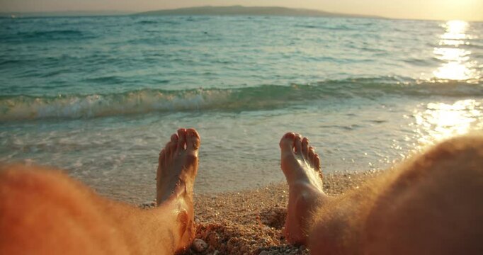 Man relaxes on pebbled beach with island view and sea waves at sunset in summer Croatia