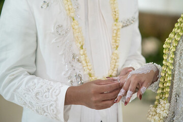 Close-up of a groom placing a wedding ring on the bride's finger during a traditional Indonesian...