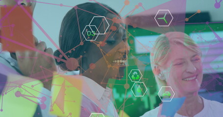 Collaborating business team placing notes on glass board in meeting room with sustainability icons