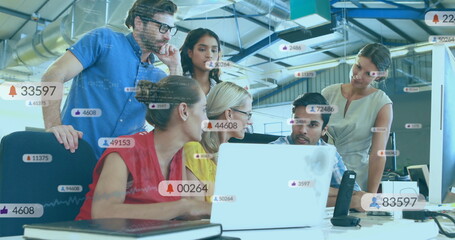 Collaborating professionals pointing at white laptop in open-plan office, with notification icons