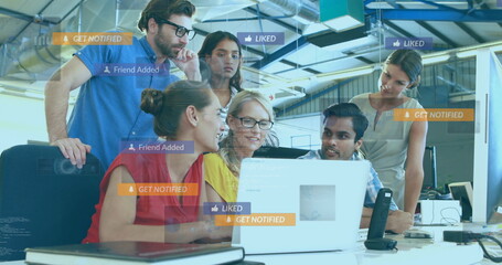 Collaborating team viewing laptop screens in open-plan office, with social media notifications