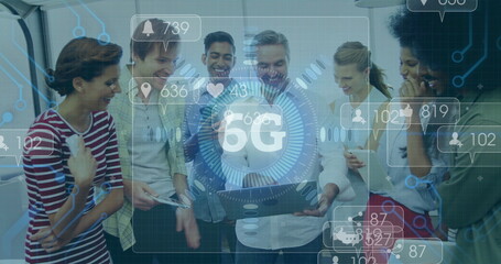 Gathering coworkers around laptop discussing in office area, with 5G icons, phone and coffee mug