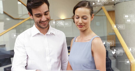 Reviewing laptop screen by two business colleagues at office stairwell, with social media icons