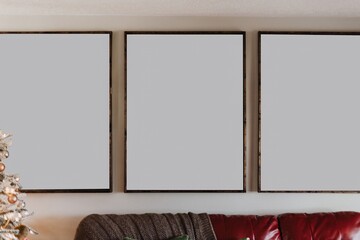 Fototapeta premium Triptych mockup with three blank frames above red leather couch in cozy holiday living room with Christmas tree and neutral modern decor