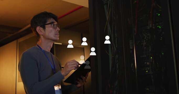 Korean technician checking server rack in server room, holding tablet and wearing lanyard