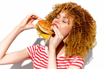 Joyful woman enjoying a delicious hamburger in a vibrant striped shirt, showcasing excitement and a...