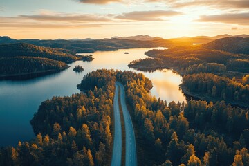 Serene lakeside road at sunset.  Aerial view of a winding asphalt road that meanders through a landscape of lush forests, calm lakes, and golden hills bathed in the warm glow of a sunset