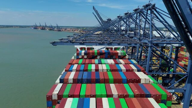 Aerial drone shot Felixstowe busy port cargo ships, shipping containers, huge cranes, loading and unloading heavy goods vehicles summer maritime business England UK.
