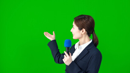 A female reporter holding a microphone in front of green background.