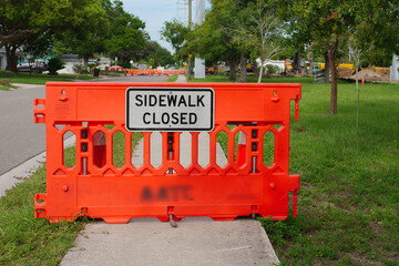 Obraz premium Sidewalk Closure with Orange Safety Barrier in Neighborhood. Bright orange safety barrier blocks a sidewalk labeled as closed in a quiet neighborhood. Highlighting urban maintenance and safety precaut