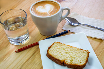 Cappuccino with latte art, pound cake and glass of water on wooden table