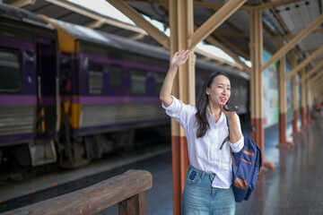 A woman is standing at a train station, waving to someone