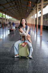 A woman is sitting on a suitcase in a train station