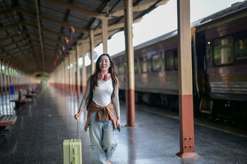 A woman is walking through a train station with a suitcase