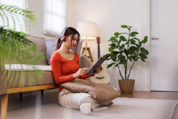 Asian Teen girl with disability wearing headphones choosing playlist for studying holding digital...