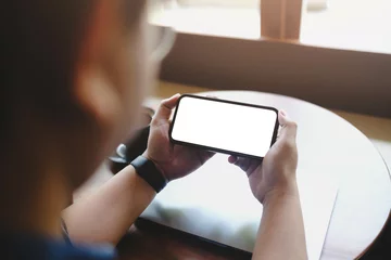 Selbstklebende Fototapeten Cappuccino A person holding a smartphone horizontally with a blank white screen. A perfect mockup for showcasing landscape video, games, or streaming content.  © Thaspol