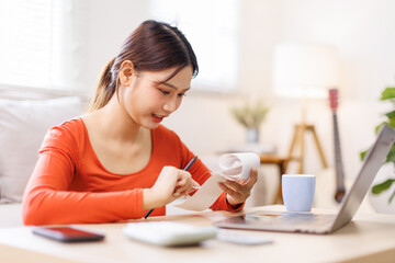 Happy asian woman manage household budget calculate expenses expenditures on machine. Smiling young...