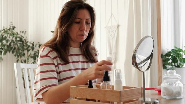 Attractive brunette mid adult woman putting on makeup looking in the mirror. Beautiful lady caring her face. 40 years old female applied cosmetics. Natural beauty and aging concept. Skin care, make-up