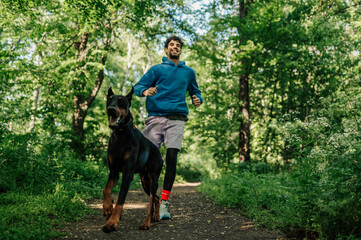 Young man running with doberman dog in forest trail