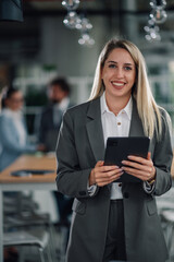 Smiling businesswoman holding tablet in modern office with colleagues working
