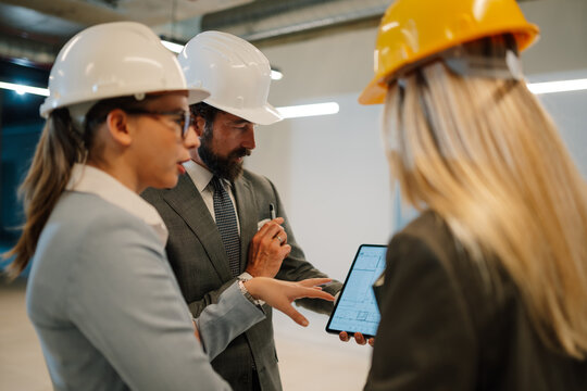 Architects and engineers discussing blueprint on tablet at construction site
