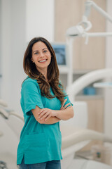 Portrait of smiling dentist posing with crossed arms in dental clinic