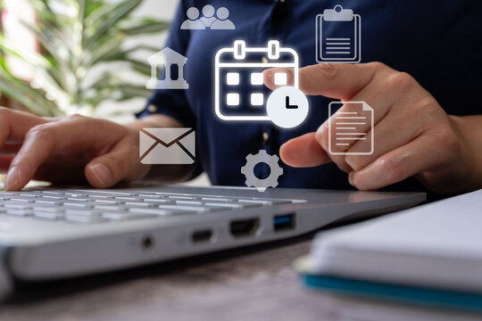 Businessman using a laptop computer with a digital calendar and icons of documents and mail floating above his hand on a desk in the office.  - Powered by Adobe